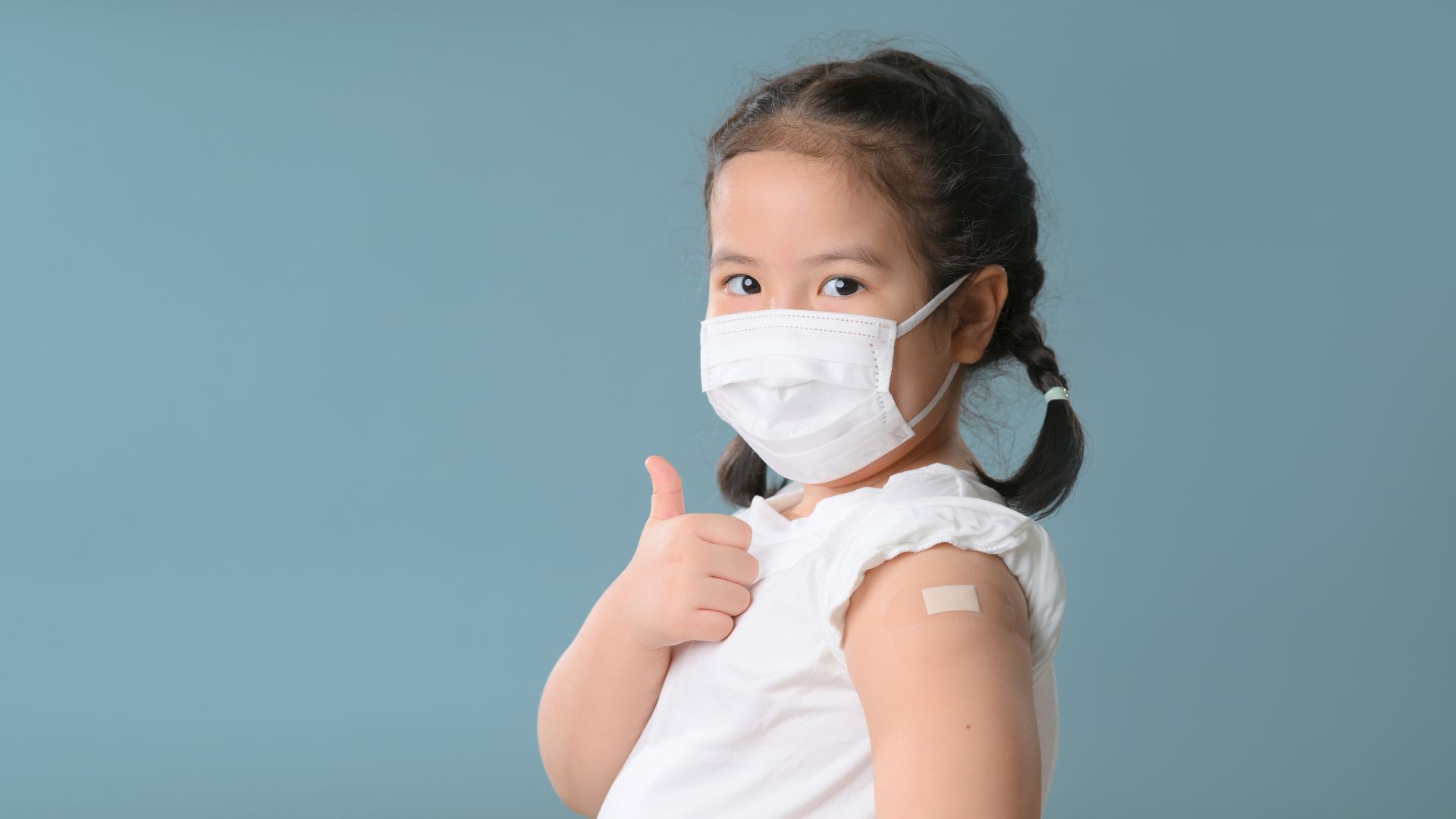 Coronavirus Vaccination Advertisement. Happy Vaccinated Little asian girl Showing Arm With Plaster Bandage After Covid 19 Vaccine Injection Posing Over Blue Background, Smiling To Camera. New normal.Covid 19 coronavirus., Blank Space